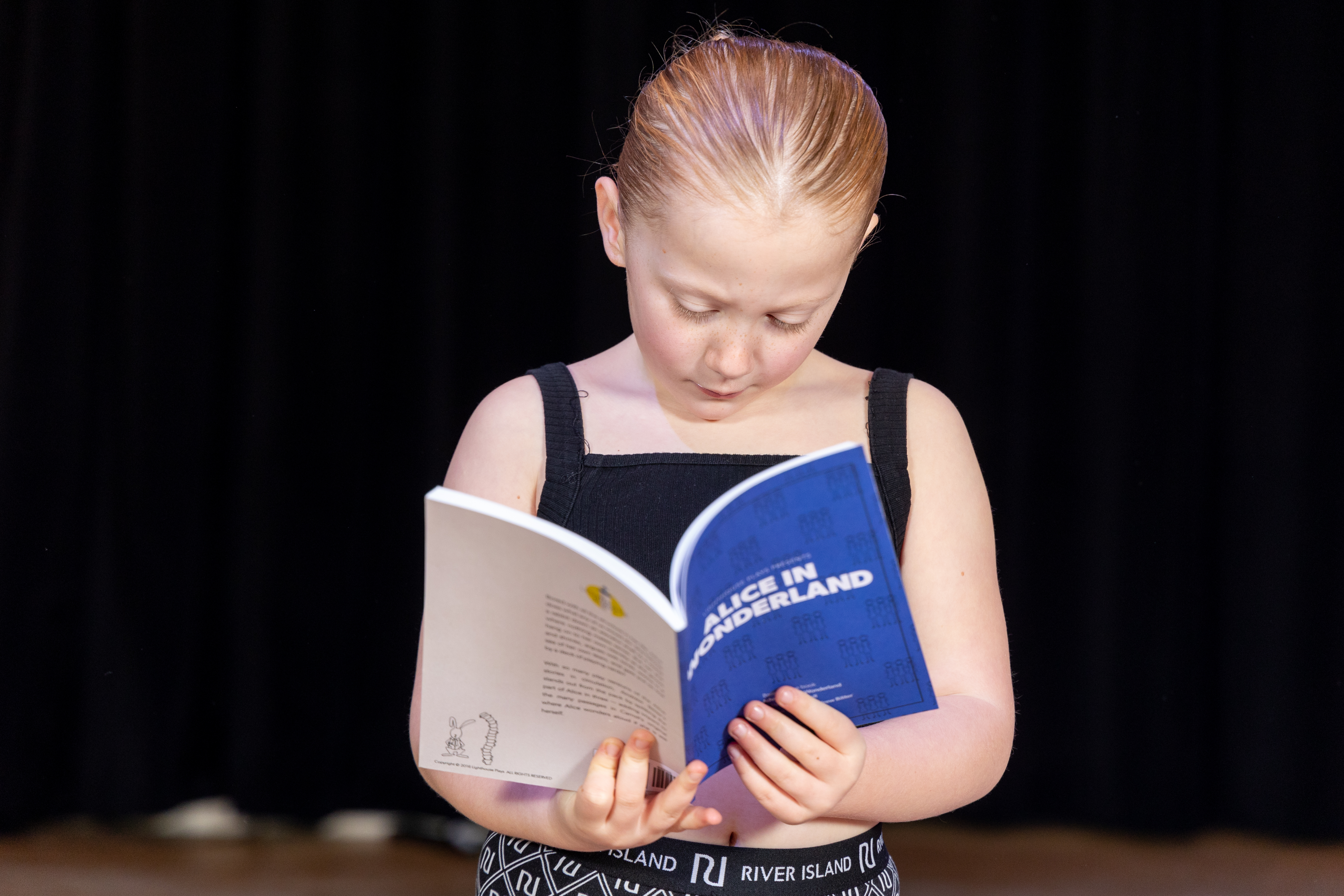 Young HI member reading Alice In Wonderland script with a blue cover